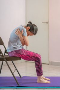 senior woman practicing chair yoga over a purple mat